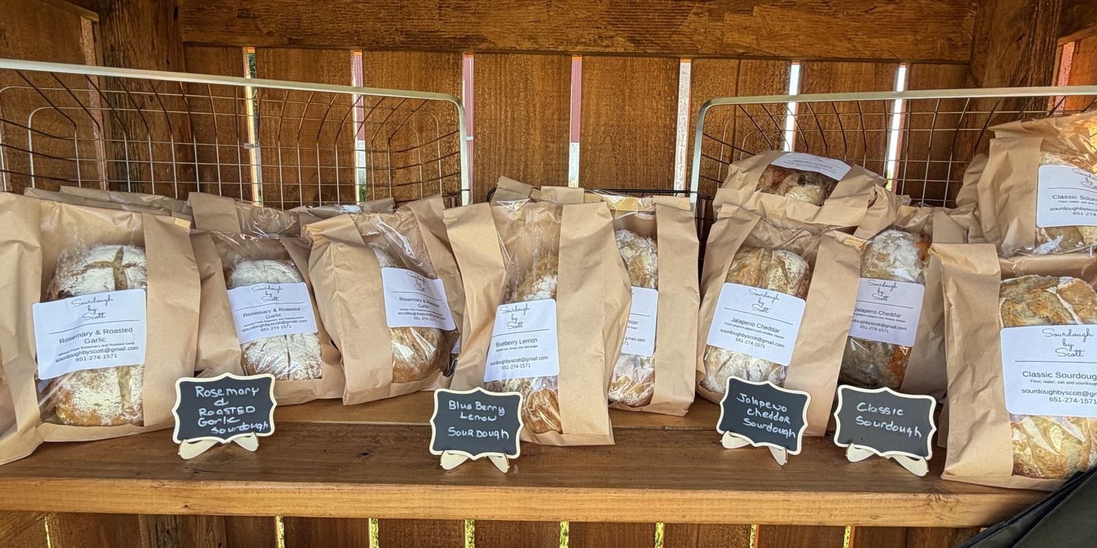 Bagged sourdough loaves with handwritten flavor tags on the shelves of the wooden honor stand